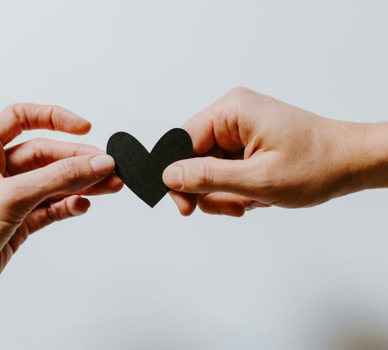 Two hands sharing a black heart between them
